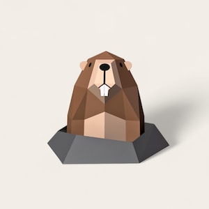 May include: A brown and beige papercraft model of a groundhog peeking out of its burrow. The burrow is made of grey paper.