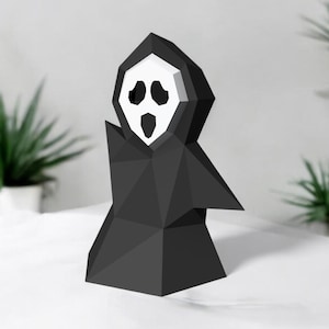 Könnte beinhalten: Eine schwarze Papierkunst-Skulptur eines Geistes mit einem weißen Gesicht und einem weit geöffneten Mund. Der Geist trägt eine schwarze Robe und hat eine dreieckige Form.