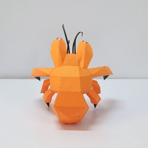 May include: An orange papercraft model of a hermit crab with black antennae. The model is made of folded paper and has a realistic appearance.