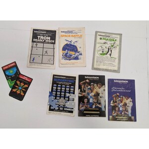 May include: A collection of eight vintage Intellivision game cartridges, including Tron Deadly Discs, Space Battle, PGA Golf, Burgertime, and Star Strike. The cartridges are in their original packaging and feature colorful artwork.