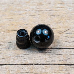 May include: Two black beads, one round and one cylindrical, with a hole in the centre. The round bead has a blue and white swirl pattern.