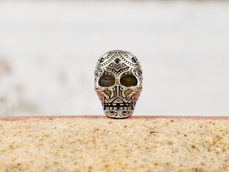 Puede incluir: Un amuleto de calavera de plata con detalles intrincados y un dise&ntilde;o estampado en blanco y negro.