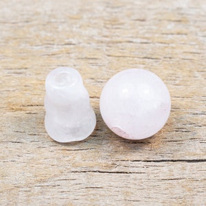 May include: Two white crystal beads, one round and one shaped like a small cone, on a wooden surface.
