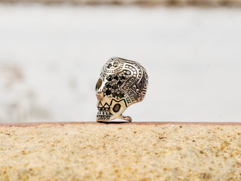 Puede incluir: Un anillo de calavera de plata con intrincados detalles en blanco y negro. La calavera est&aacute; adornada con peque&ntilde;as piedras negras.