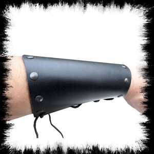May include: Black leather arm guard with metal rivets and a lace-up closure.