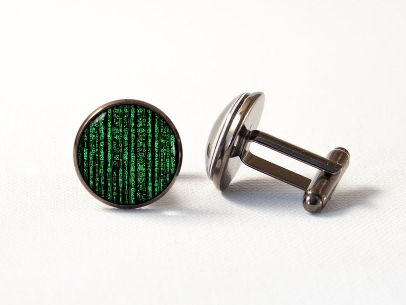 May include: A pair of cufflinks with a Matrix-inspired design. The round, black cufflinks feature a green digital rain pattern on a black background. The cufflinks have a gunmetal finish and a classic T-bar closure.