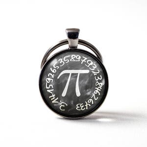 May include: A silver keychain with a round black and white charm featuring the mathematical symbol pi and the first digits of pi around the edge.