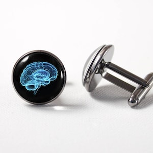 May include: A pair of cufflinks with a black background and a blue outline of a brain. The cufflinks are silver.