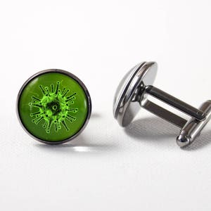 May include: A pair of silver cufflinks with a green glass cabochon featuring a stylized image of a virus.