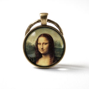 May include: A bronze-colored pendant featuring a round glass cameo with a reproduction of the Mona Lisa painting. The cameo is set in a decorative frame.