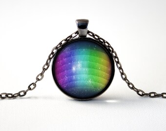 Puede incluir: Un collar con un colgante de vidrio arcoíris con una cadena plateada. El colgante presenta un diseño de galaxia con un patrón de rayas arcoíris.