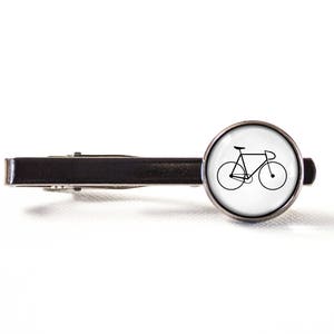 May include: A silver tie clip featuring a black and white outline of a bicycle on a white background.