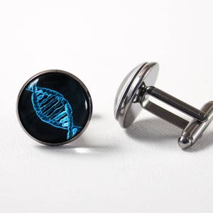 Op de afbeelding: Een paar zilveren manchetknopen met een zwarte achtergrond en een blauw DNA-helixontwerp.