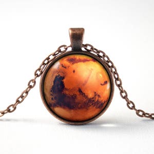 Könnte beinhalten: Eine Halskette aus Kupferkette mit einem runden Glasanhänger, der ein detailliertes Bild des Planeten Mars zeigt. Der Anhänger ist dunkelorange mit braunen und roten Markierungen.