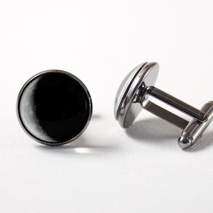 May include: A pair of silver cufflinks with a black and white crescent moon design.