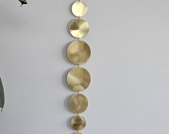 Könnte beinhalten: Ein goldfarbener Wandbehang aus Metall mit einer Reihe runder Scheiben in verschiedenen Größen, die an einer Kette hängen.