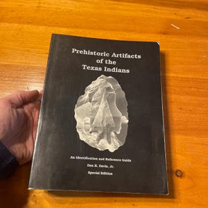 May include: A book titled "Prehistoric Artifacts of the Texas Indians" with a black cover and a white illustration of a stone artifact. The book is a special edition and an identification and reference guide by Dan R. Davis, Jr.
