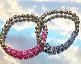 May include: Two gold beaded bracelets with the words "BRIDES" and "BRIDESMAID" spelled out in pink and white beads.