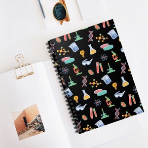 May include: A black spiral notebook with a colorful science pattern. The pattern includes beakers, test tubes, microscopes, light bulbs, and DNA strands.