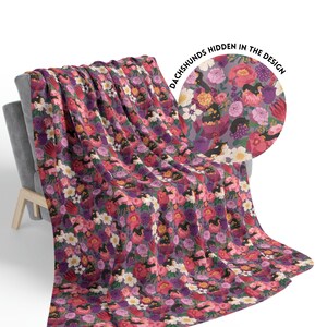 May include: A purple, pink, and white floral patterned throw blanket with a hidden dachshund design. The text "Dachshunds Hidden in the Design" is printed in a circle on the blanket.