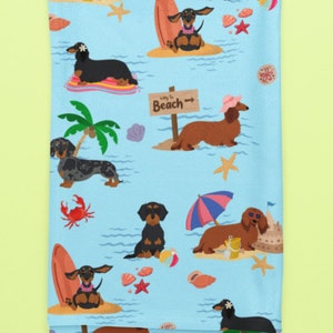 May include: A blue beach towel with a repeating pattern of dachshund dogs enjoying summer activities. The dogs are wearing sunglasses, hats, and leis. Some are surfing, others are relaxing under umbrellas, and some are building sandcastles. The text "Way to Beach" is on a sign.