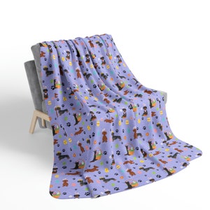 May include: A purple fleece throw blanket with a repeating pattern of dachshund dogs holding Easter baskets filled with colorful eggs. The dogs are brown and black with long ears and short legs. The background is a light purple with paw prints and small flowers.
