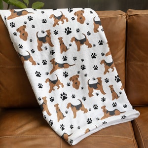 Puede incluir: Manta de forro polar blanca con un patrón repetido de Airedale Terriers marrones y negros y huellas de patas negras.
