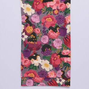 May include: A purple fabric tea towel with a floral pattern featuring black and tan dachshund dogs. The flowers are pink, red, white, and yellow.