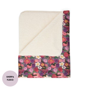 May include: A soft, plush sherpa fleece throw blanket with a floral print featuring pink, purple, and white flowers and birds. The blanket has a white sherpa fleece backing.