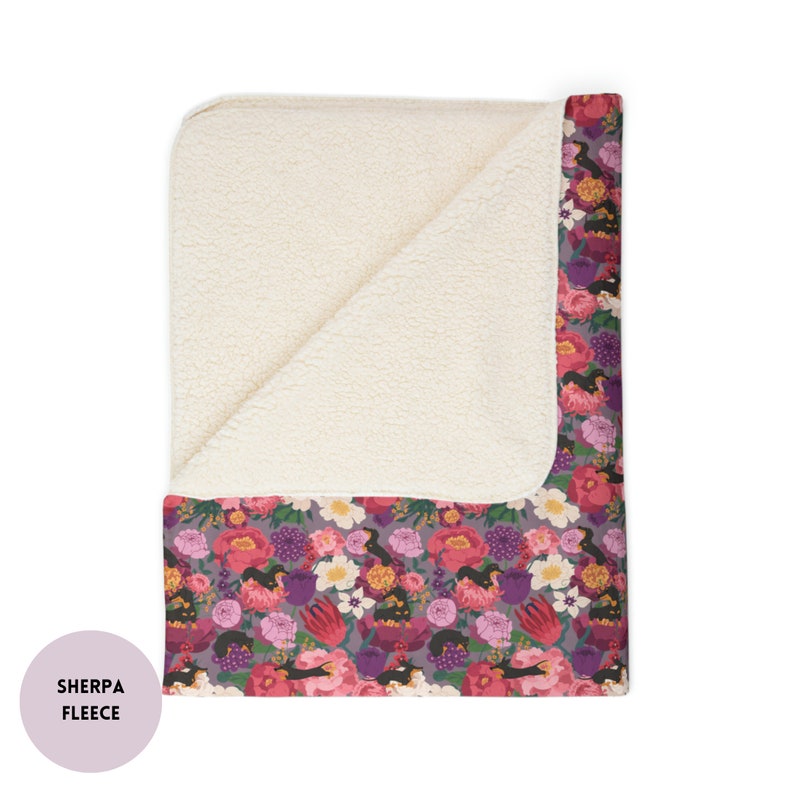 May include: A soft, plush sherpa fleece throw blanket with a floral print featuring pink, purple, and white flowers and birds. The blanket has a white sherpa fleece backing.