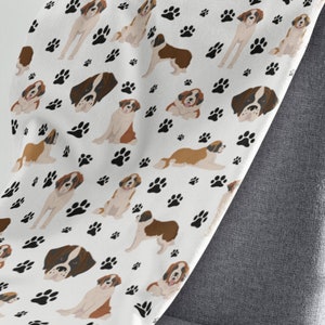 May include: White fleece blanket with a repeating pattern of brown and white Saint Bernard dogs and black paw prints.