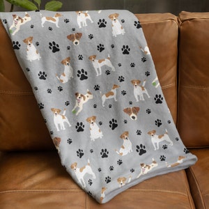 Peut inclure: Une couverture en polaire grise avec un motif répété de Jack Russell terriers bruns et blancs et d'empreintes de pattes noires.
