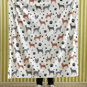 Peut inclure: Une couverture en polaire blanche avec un motif r&eacute;p&eacute;t&eacute; de chiens bergers australiens bleus et bruns et d'empreintes de pattes noires.