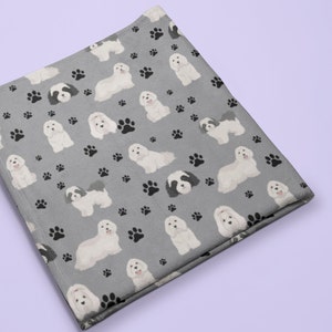 K&ouml;nnte beinhalten: Eine graue Fleece-Decke mit einem sich wiederholenden Muster aus wei&szlig;en Hunden und schwarzen Pfotenabdr&uuml;cken.