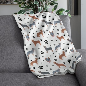 Peut inclure: Une couverture en polaire blanche avec un motif r&eacute;p&eacute;t&eacute; de chiens bergers australiens bleus et bruns et d'empreintes de pattes noires.