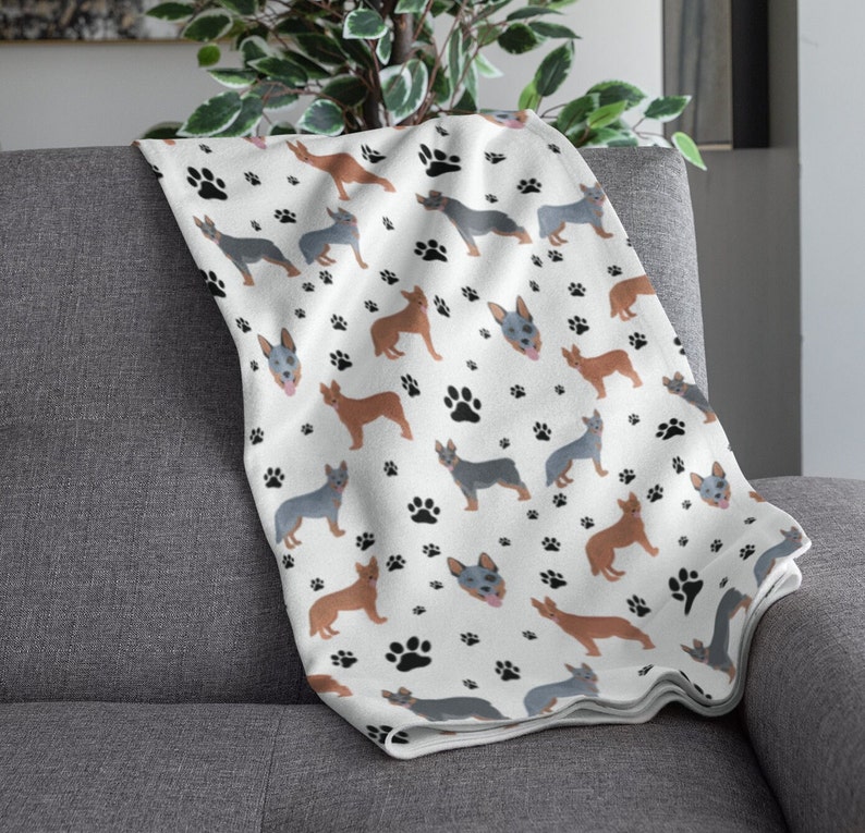 Peut inclure: Une couverture en polaire blanche avec un motif r&eacute;p&eacute;t&eacute; de chiens bergers australiens bleus et bruns et d'empreintes de pattes noires.