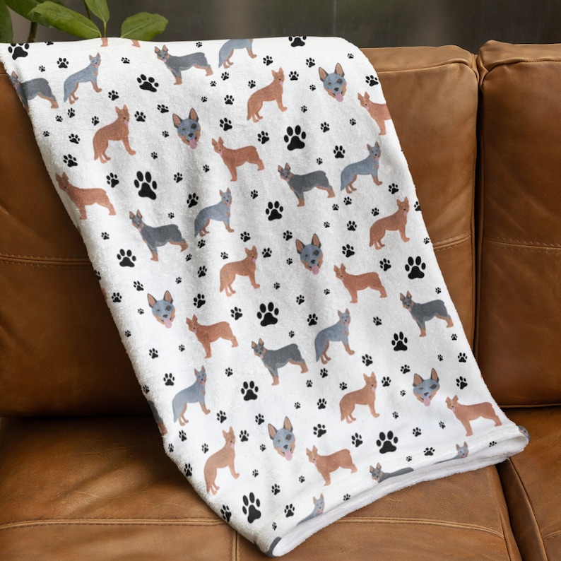 Peut inclure: Une couverture en polaire blanche avec un motif r&eacute;p&eacute;t&eacute; de chiens bergers australiens bleus et bruns et d'empreintes de pattes noires.