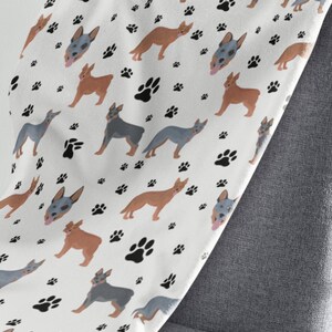 Peut inclure: Une couverture en polaire blanche avec un motif r&eacute;p&eacute;t&eacute; de chiens bergers australiens bleus et bruns et d'empreintes de pattes noires.