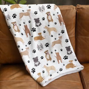 May include: White fleece throw blanket with a repeating pattern of brown and tan pit bull dogs and black paw prints.