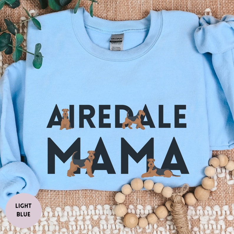 May include: Light blue sweatshirt with the text "Airedale Mama" in black. The text is surrounded by four brown and black Airedale Terrier dogs.