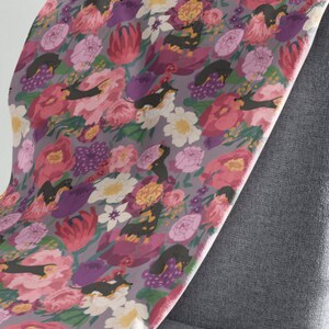 May include: A fabric with a repeating pattern of black and tan dachshund dogs in a field of pink, purple, and white flowers. The fabric is draped over a gray chair.