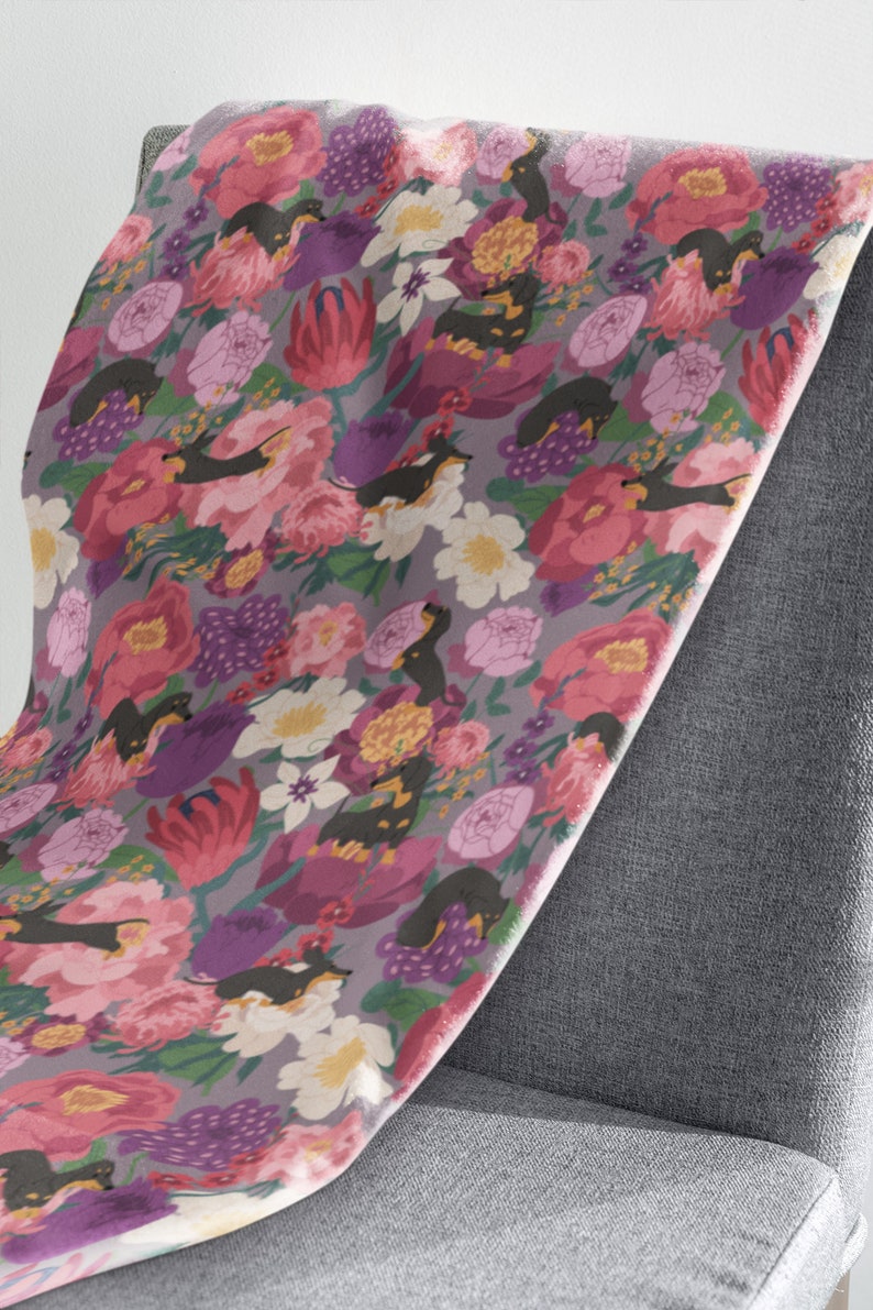 May include: A fabric with a repeating pattern of black and tan dachshund dogs in a field of pink, purple, and white flowers. The fabric is draped over a gray chair.