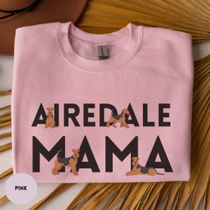 May include: Pink sweatshirt with the text "Airedale Mama" in black lettering. The text is surrounded by four small illustrations of Airedale Terriers.