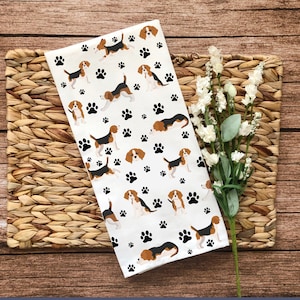 May include: White kitchen towel with a repeating pattern of brown and white beagle dogs and black paw prints.