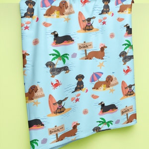 May include: A blue and white beach themed fabric with a repeating pattern of dachshunds wearing sunglasses, hats, and holding surfboards. The text "Way to Beach" is repeated on the fabric.