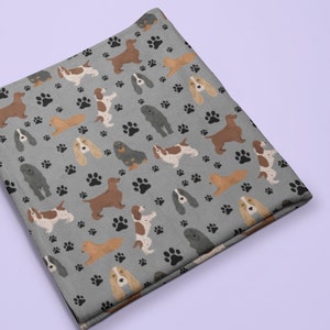 Può includere: Una coperta in pile grigia con un motivo ripetitivo di cani Cocker Spaniel marroni, neri e bianchi e impronte di zampe nere.