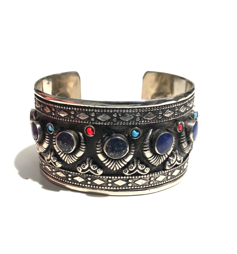 May include: A silver cuff bracelet with intricate designs and blue, red, and turquoise gemstones.