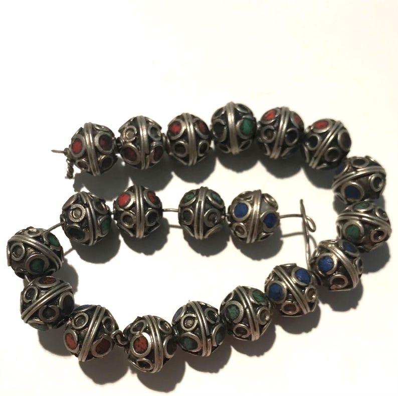 May include: A strand of silver beads with intricate designs and colorful accents. The beads are round and have a textured surface. The colors of the accents are red, blue, and green.