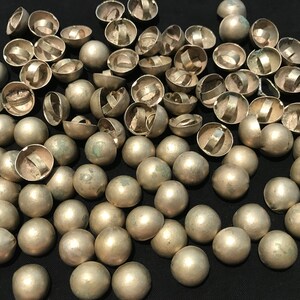 May include: A large group of silver-toned metal dome-shaped buttons with a ring on the top. The buttons are scattered on a black surface.