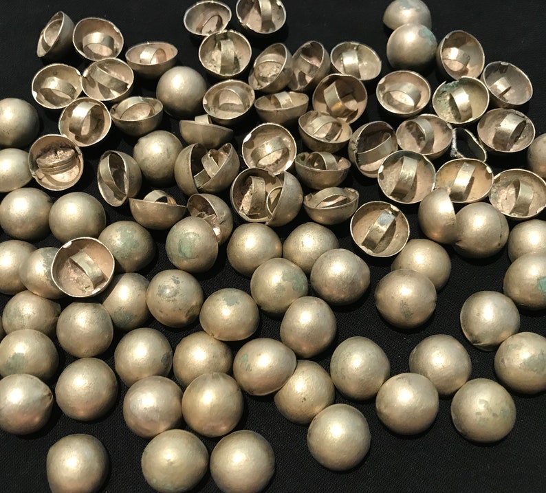 May include: A large group of silver-toned metal dome-shaped buttons with a ring on the top. The buttons are scattered on a black surface.
